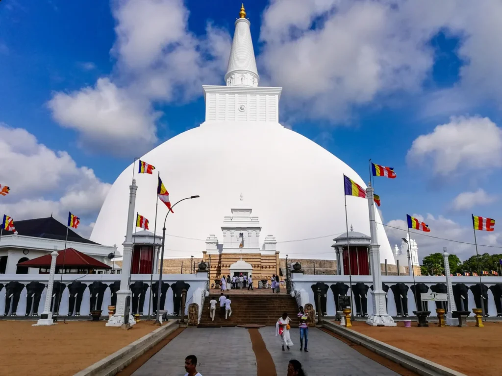White Ruwanwelisaya stupa with visitors, flags and temple buildings in Anuradhapura, Sri Lanka