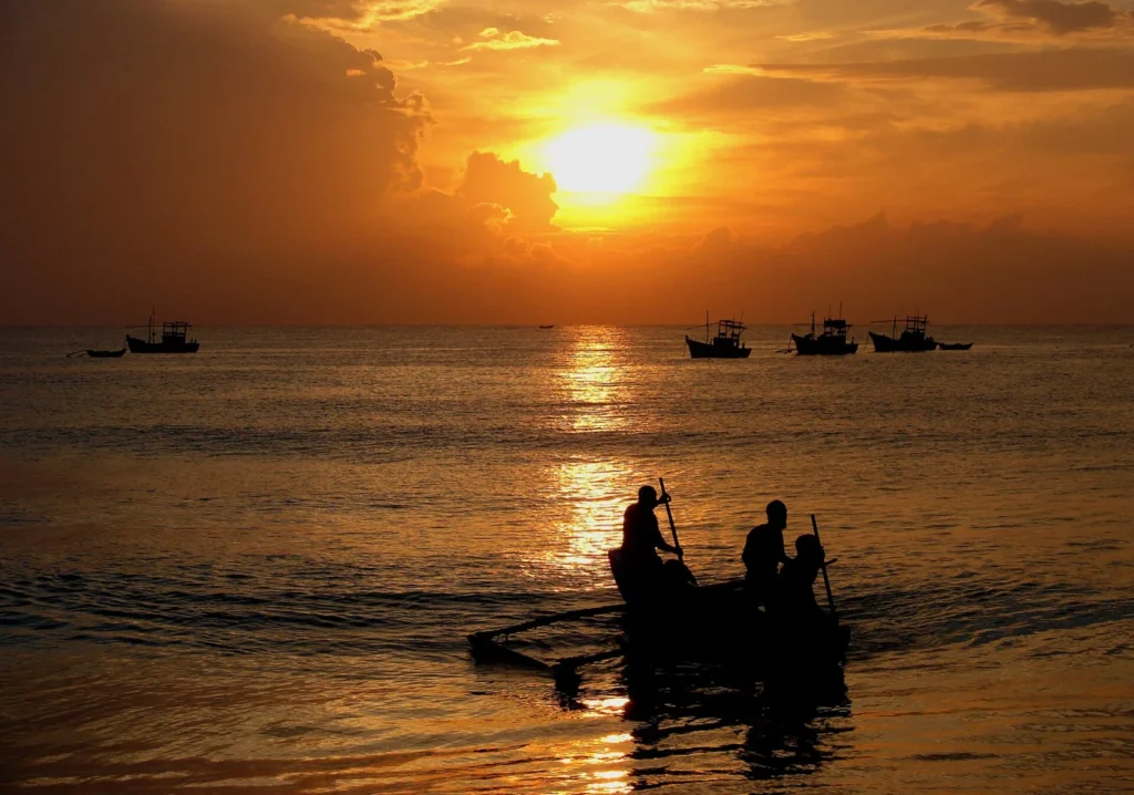 Silhouetted fishing boats and people on the sea beneath an orange sunset at Batticaloa, Sri Lanka