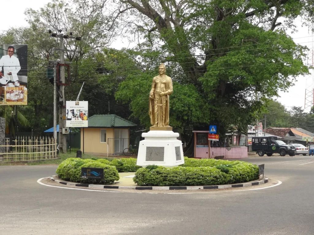 Golden statue on a plinth beside a road and leafy trees in Habarana, Sri Lanka
