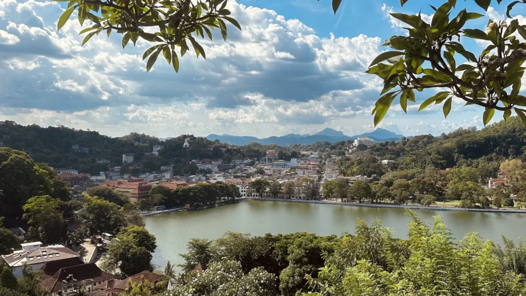 Kandy Lake surrounded by city buildings and green hills, framed by tree branches, Sri Lanka