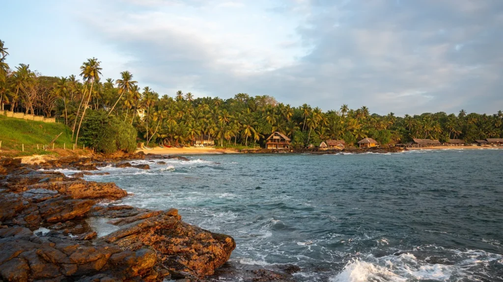 Rocky shoreline, blue water and a palm-lined sandy beach at Goyambokka near Tangalle, Sri Lanka