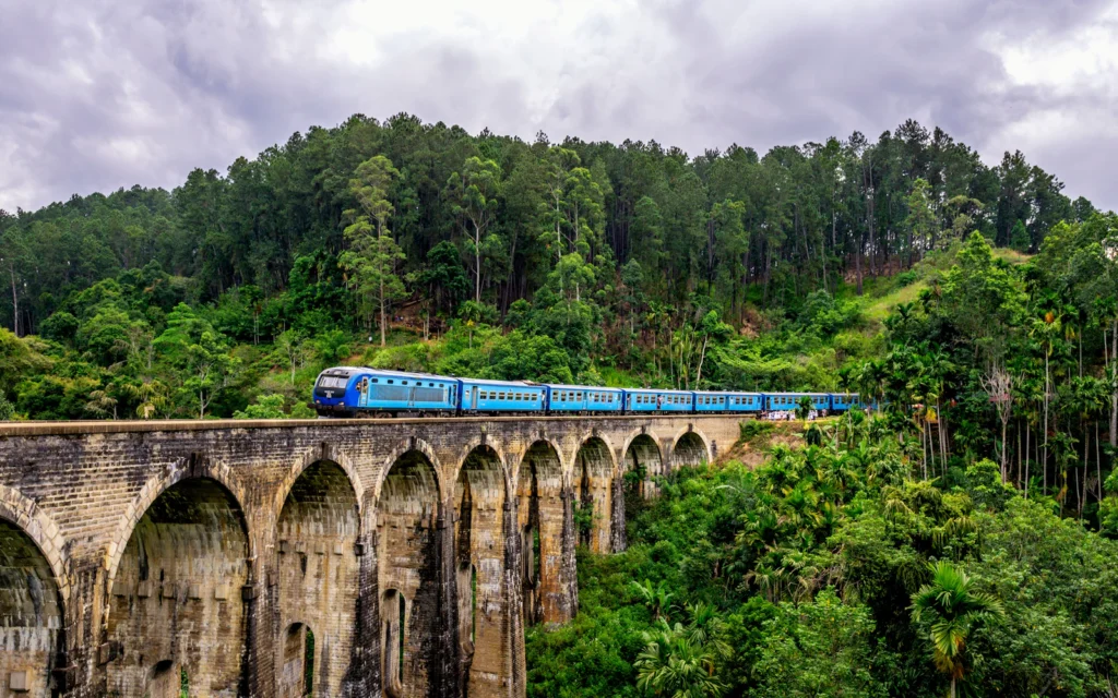 Blue passenger train crossing the stone Nine Arch Bridge amid green hills near Ella, Sri Lanka